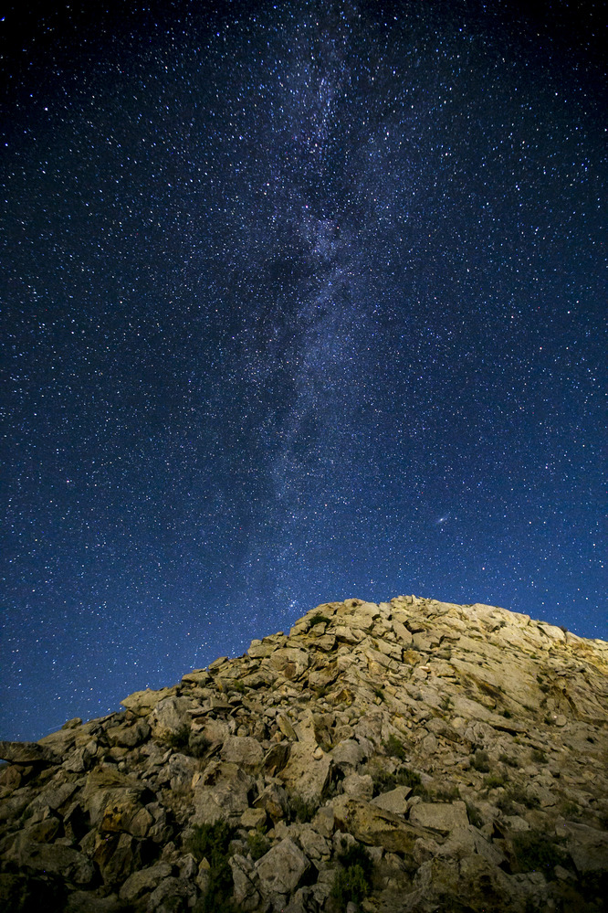The Milky Way rises through the sky from the point of a rocky hill.
