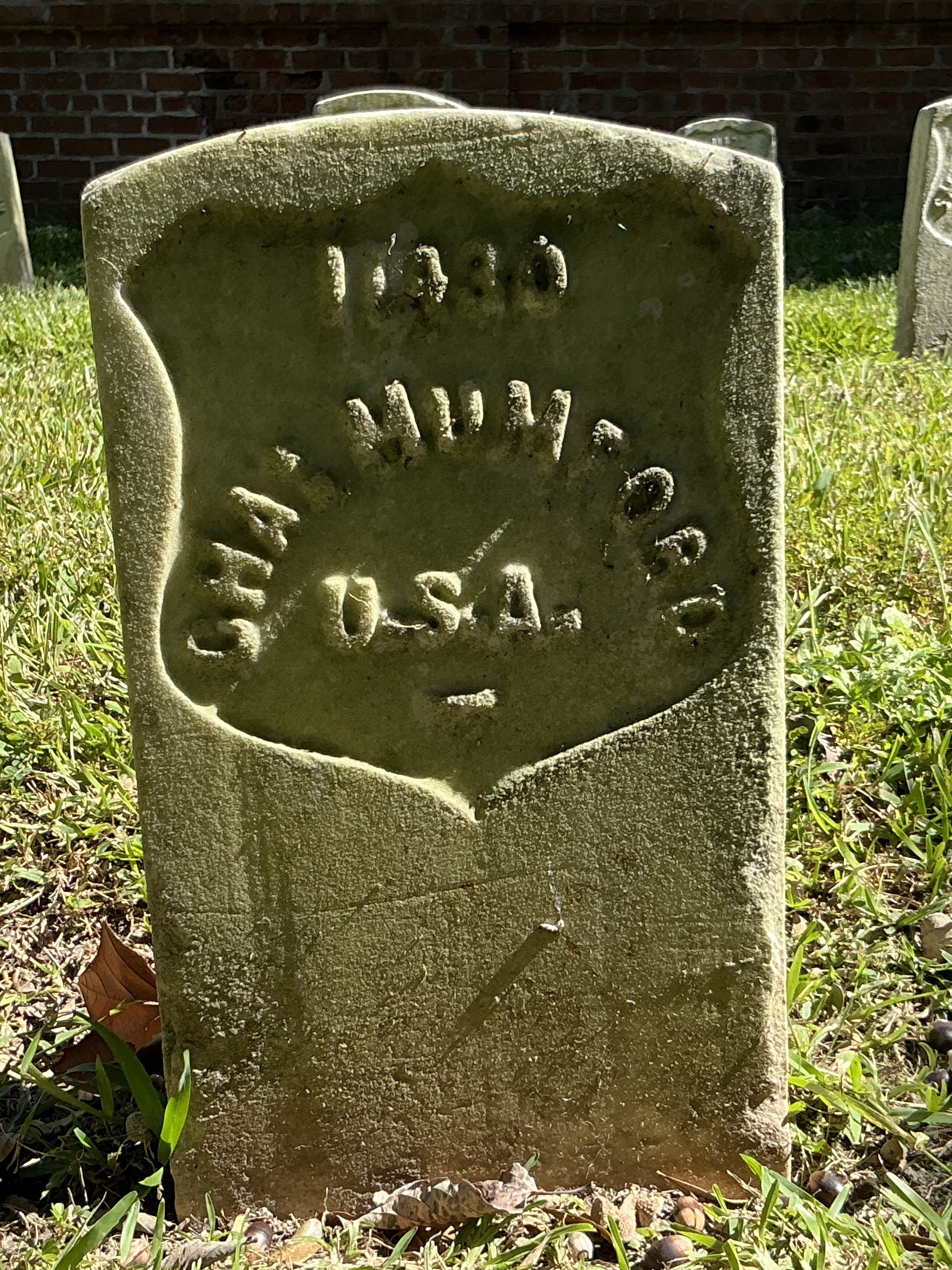 Front of historic upright marble headstone with recessed shield with recessed lettering face.