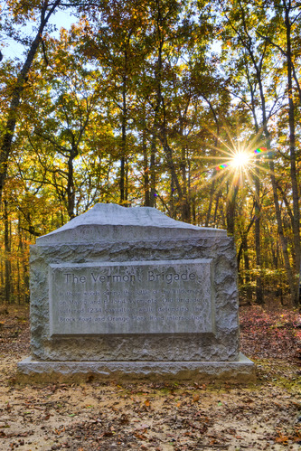 A rectangular stone monument in the woods, the monument has the text Vermont Brigade on it and is topped by the outline of a mountain. 