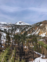 A steep alpine valley with sparse patches of snow beneath a snow-covered volcanic peak.