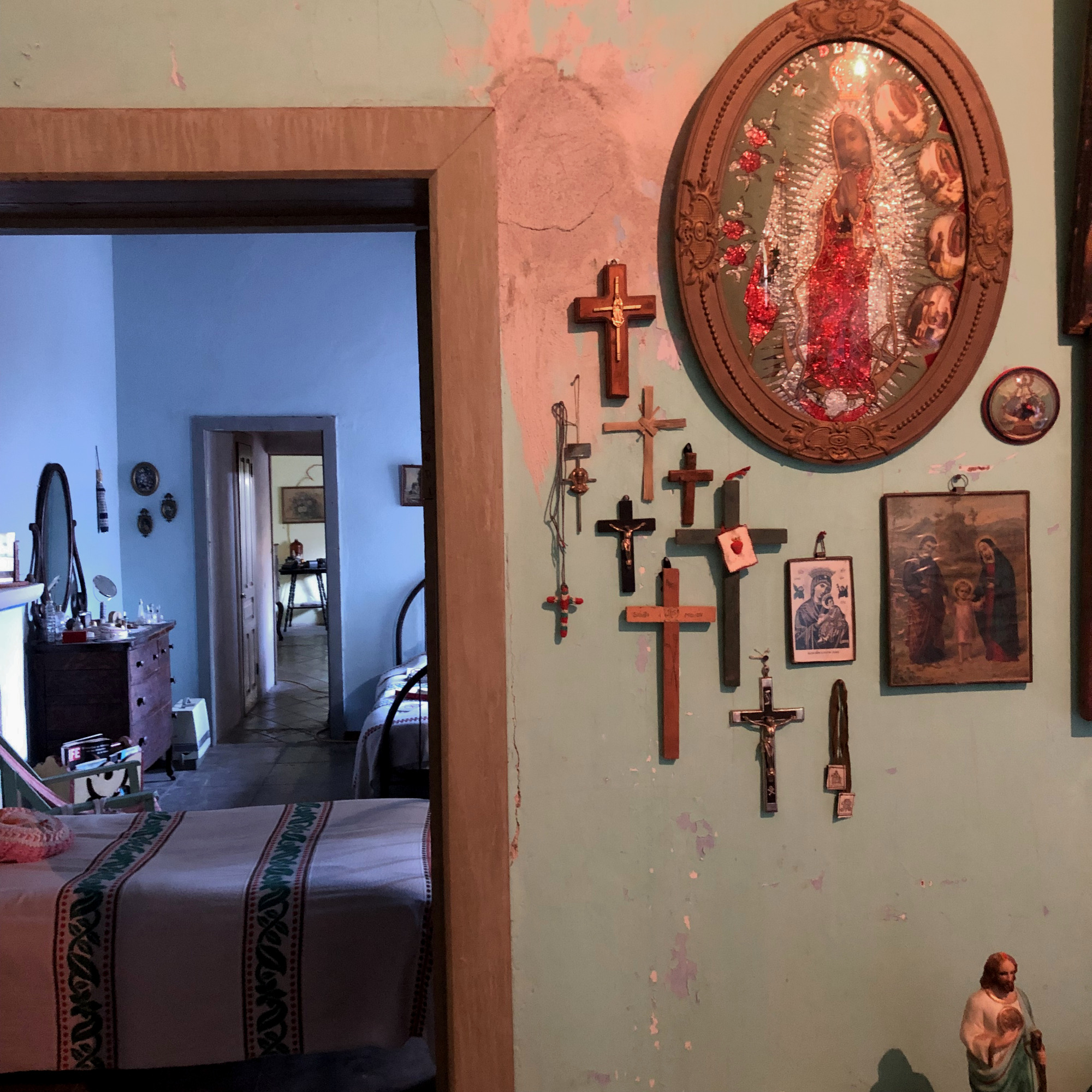 Inside of a house, a hallway has many crosses and depictions of the Virgin Mary and Joseph