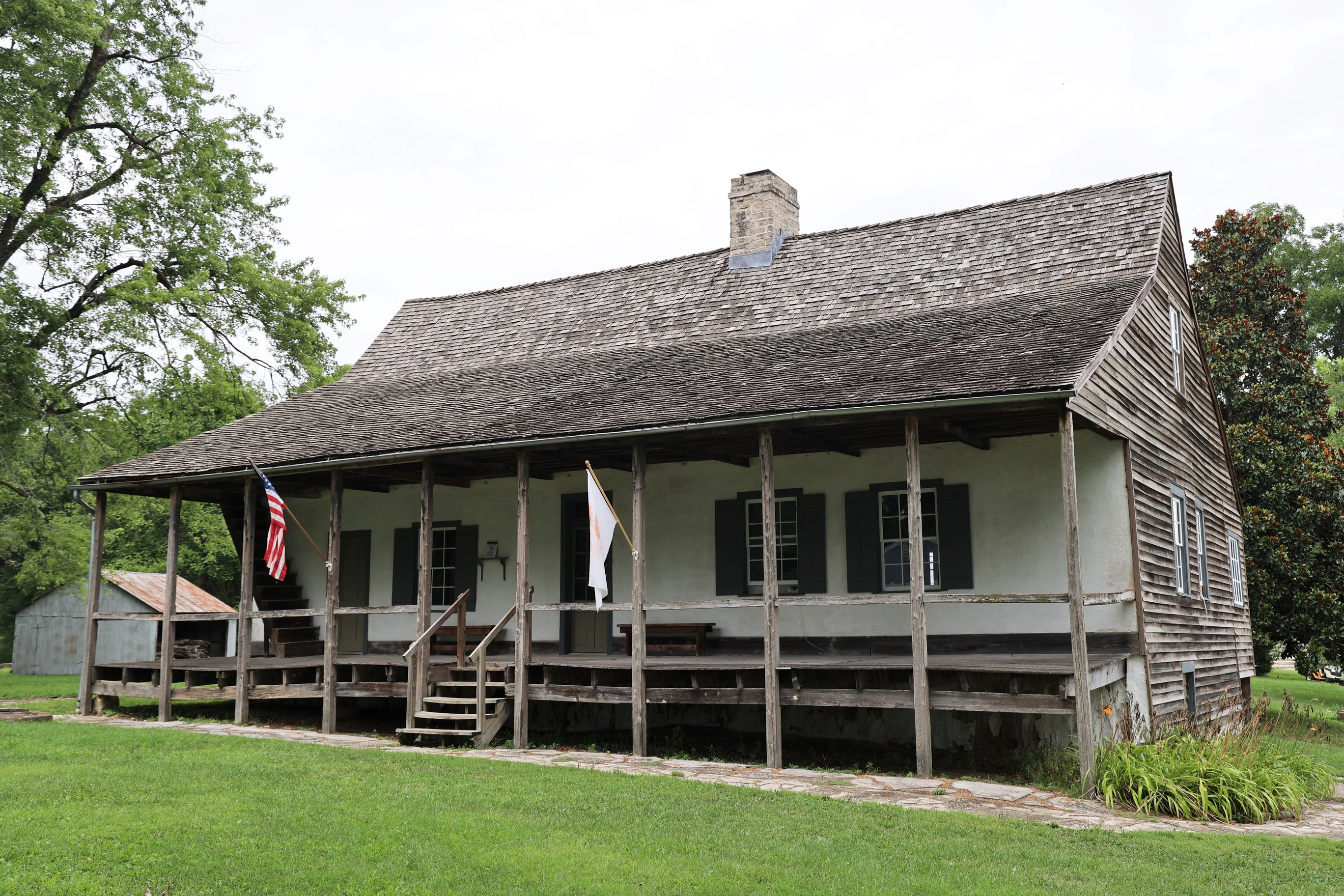 A house with a covered front porch, white front, plain wood siding and shingles.