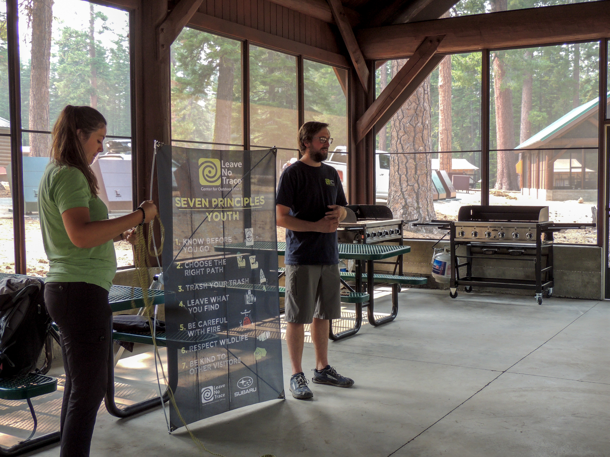 Subaru Leave No Trace Trainers standing next to a sign on the Seven Principles of Leave No Trace for youth inside a picnic pavillion at the Volcano Adventure Camp
