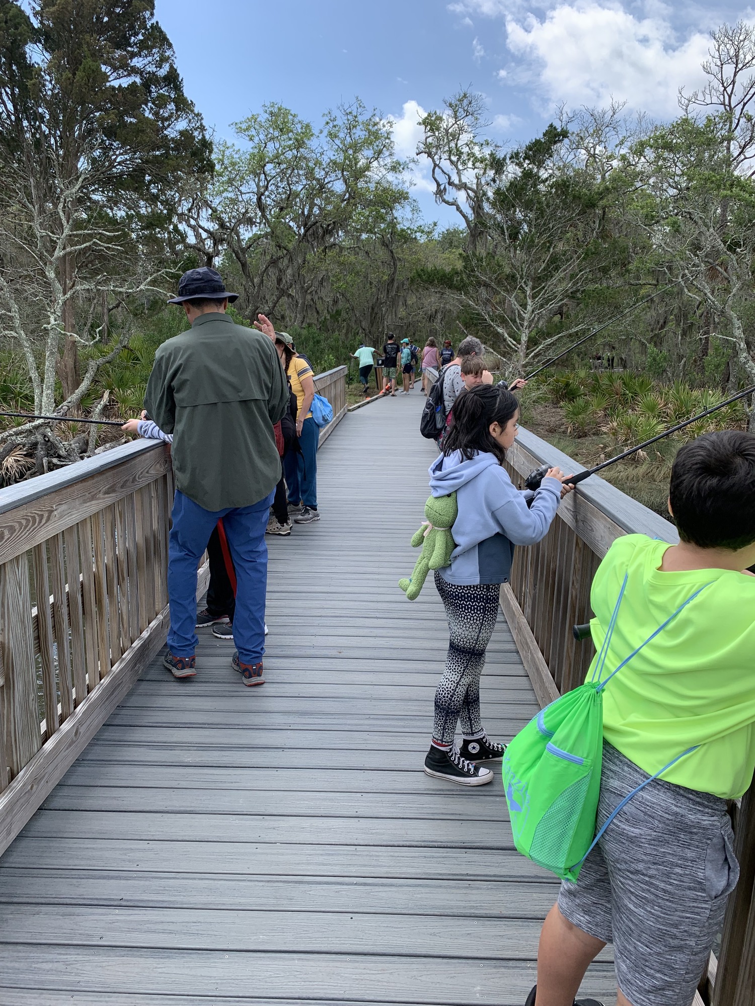people with fishing l=pols on long wood pier in nature