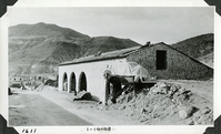 This is an historic black and white photograph from the Scotty's Castle Historic Photograph Collection, Death Valley National Park of Scotty's Castle Stables, looking west at north wing. This is immediately after construction with concrete sacks stacking inside. Scotty's Castle Main House and Annex in distance. January 14, 1928. Photographed by Mat Roy Thompson.