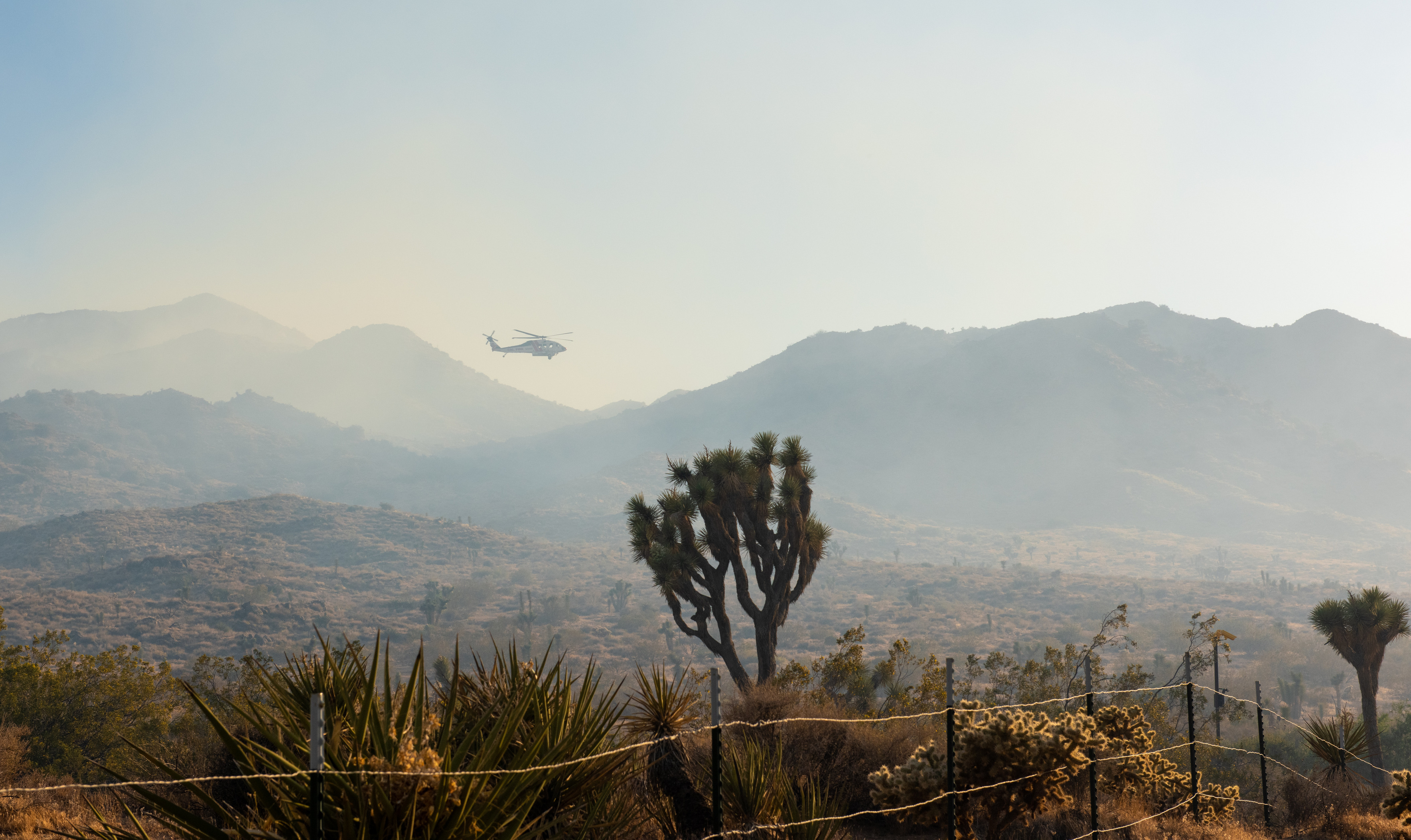 A helicopter flying above smoke and a desert landscape. 