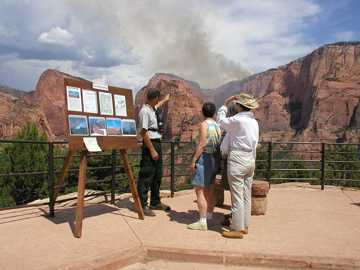 PIO points to smoke in the distance and explains wildland fire to park visitors. 