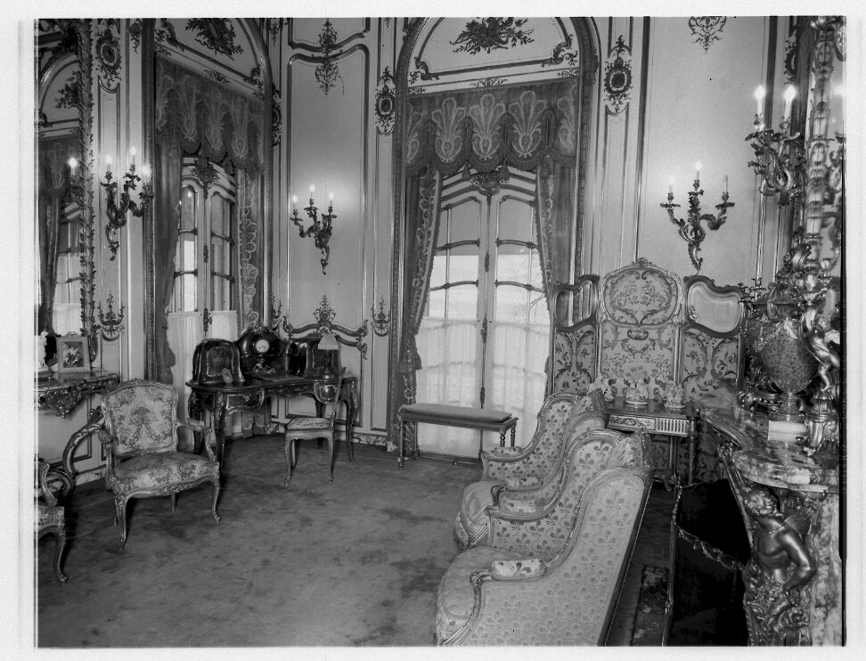  Small room decorated with marble objects, gilded furniture, and a screen.