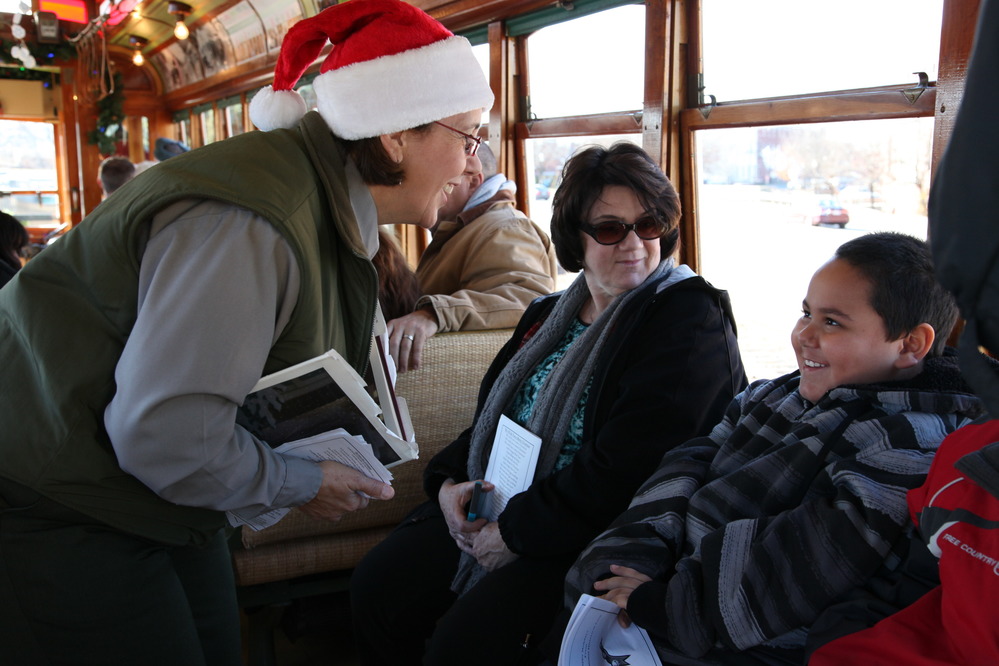  Park ranger in Santa hat holding a book and talking to children on a trolley.