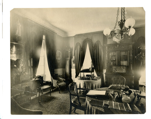 Black and white photograph of 19th century study, brightly lit by three windows.