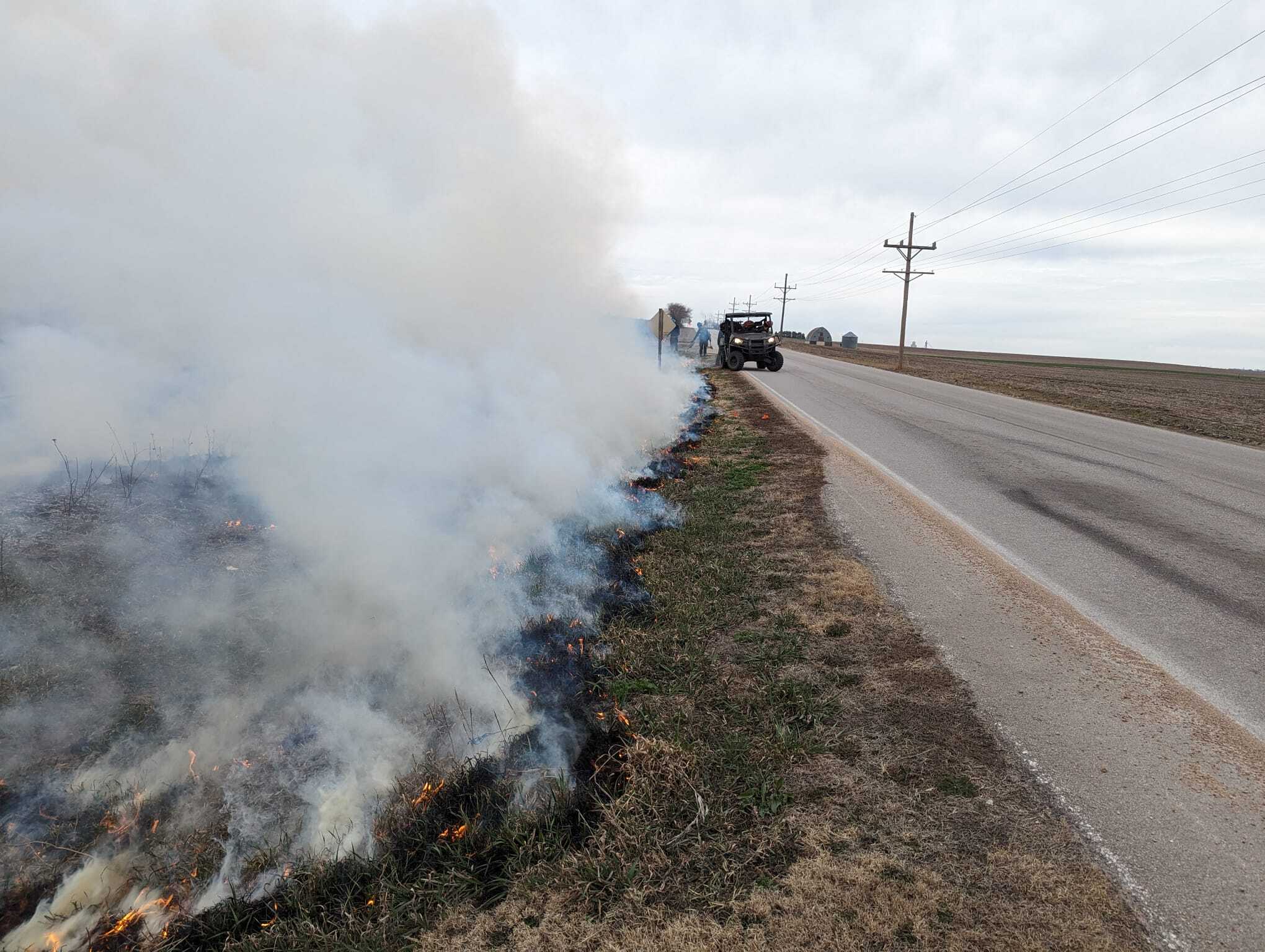 Smoke, seen right next to the road, blows away from the road. A UTV is stationed to direct traffic if weather conditions change.