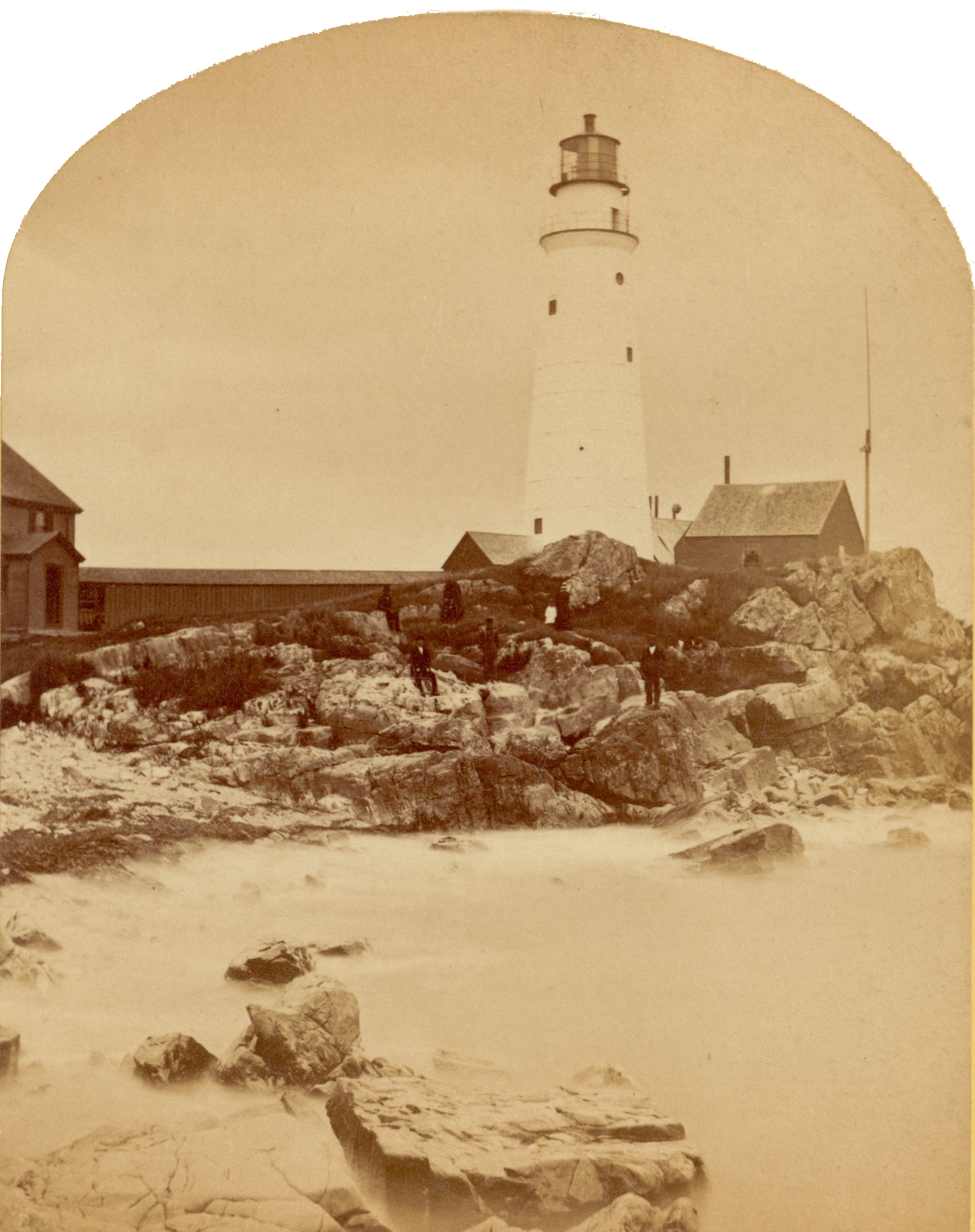 Boston Light House in Boston Harbor, with people standing and sitting on large rocks in front of it.