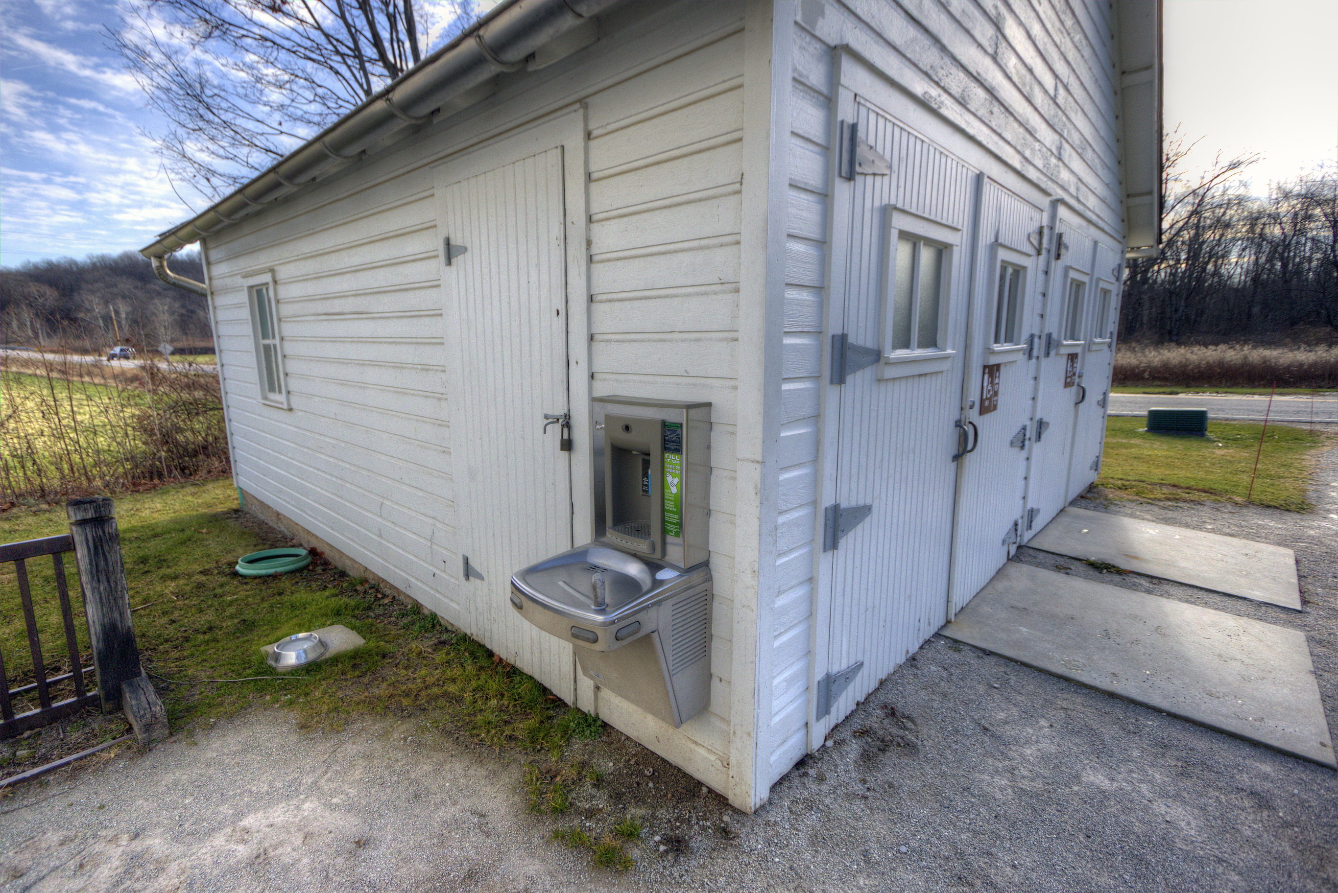 Exterior of white restroom building with barn style doors. A water fountain is located around the left corner of the building from the doors.