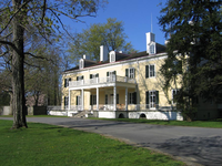A curving entrance road passes in front of a two-story yellow mansion, lined with windows 