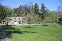 Several fruit trees of varying age and condition grow in an area of short turf in front of the stone garage.