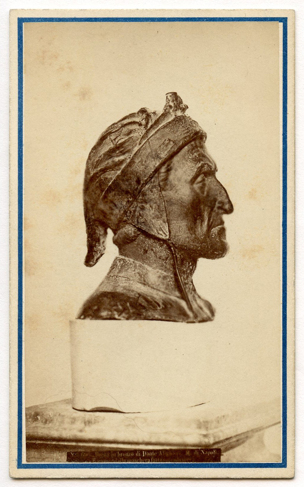 Profile view of portrait bust. Subject wears a cloth cap with two strings, one on each side of his head. Label with "No. 693. Busto in Bronzo di Dante Alighieri. M. di Napoli./ Ricatavodalla maschera fatta sui cadaverre." barely visible placed beneath bust.