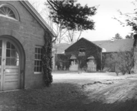 The ivy-covered garage is visible across a driveway, past a cement block garage with an arched doorway. 