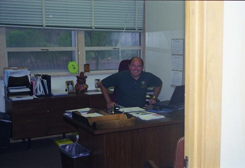 Color Photos of administration personnel. Man seated at desk.