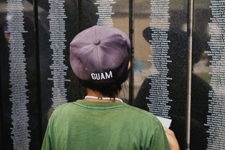 A young boy with his back to the camera looks at a wall covered in black plaques with names engraved on them.