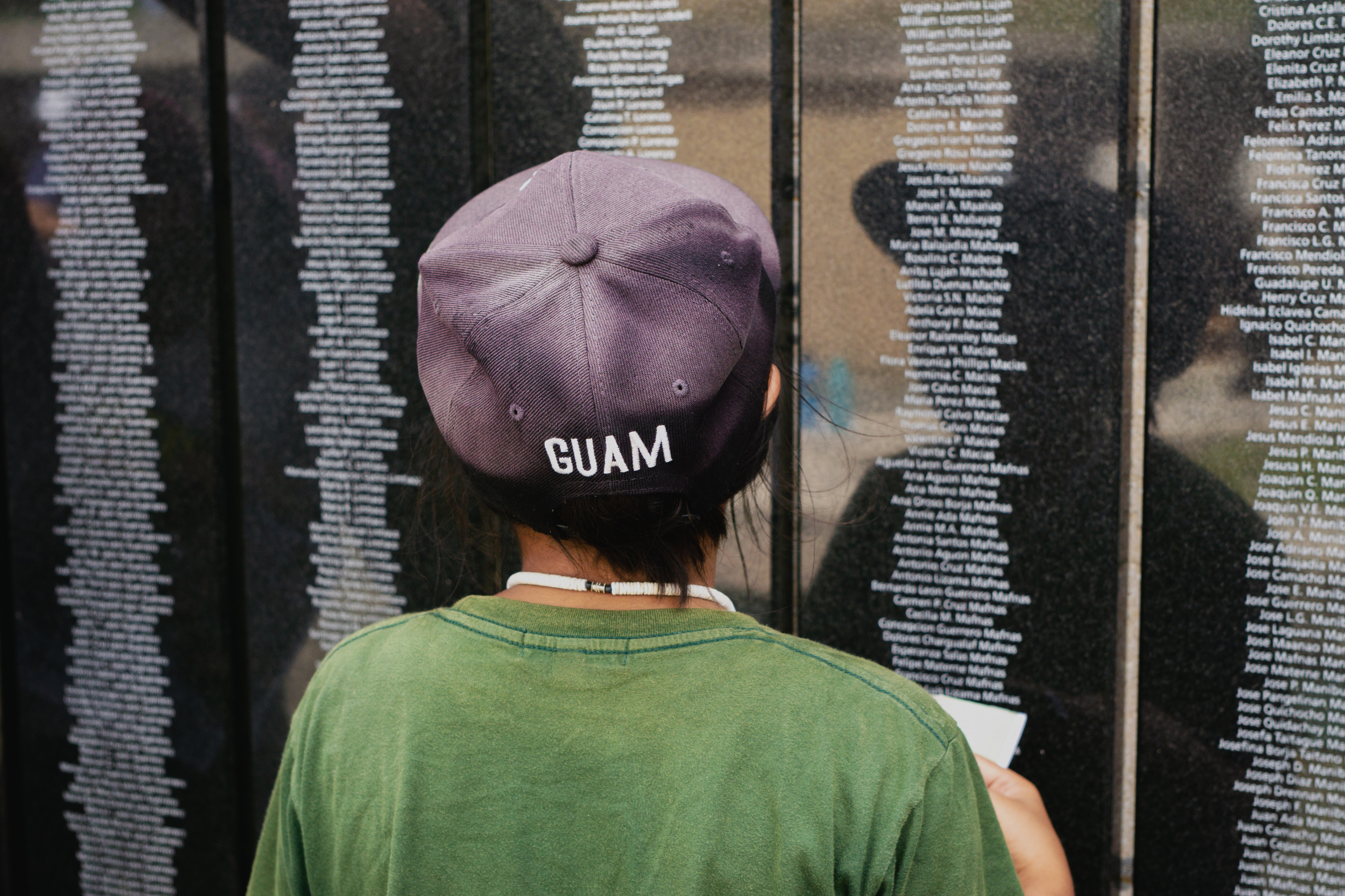 A young boy with his back to the camera looks at a wall covered in black plaques with names engraved on them.
