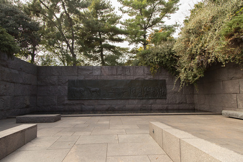 Brass sculpture embedded in wall of funeral procession hung over still pool