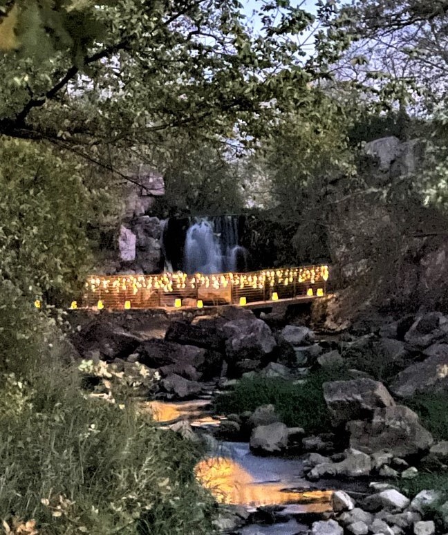 Lights on a bridge in front of a waterfall at night
