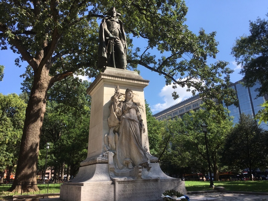 A statue of Commodore John Barry on top of a tall pedestal that depicts the figure of Victory.