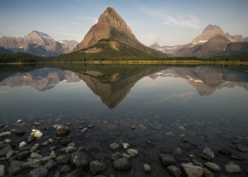 Grinnell Peak reflects in the calm waters of Swiftcurrent Lake on a beautiful sunrise at Many Glacier