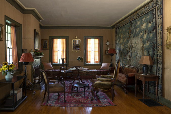 Room with three bright windows and several elaborate chairs. A large tapestry hangs on one wall.