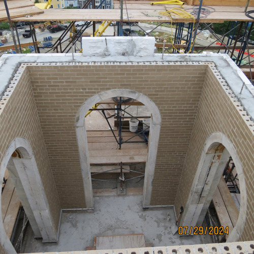 A brick wall with an arch with two walls perpendicular to it, also with arches. Scaffolding surrounds the walls. 