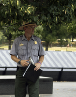 A park ranger at the Korean War Memorial stands under a tree and surveys the grounds. 