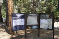 A tri-panel informational board sits in the foreground. In the background are trees and rocks. 