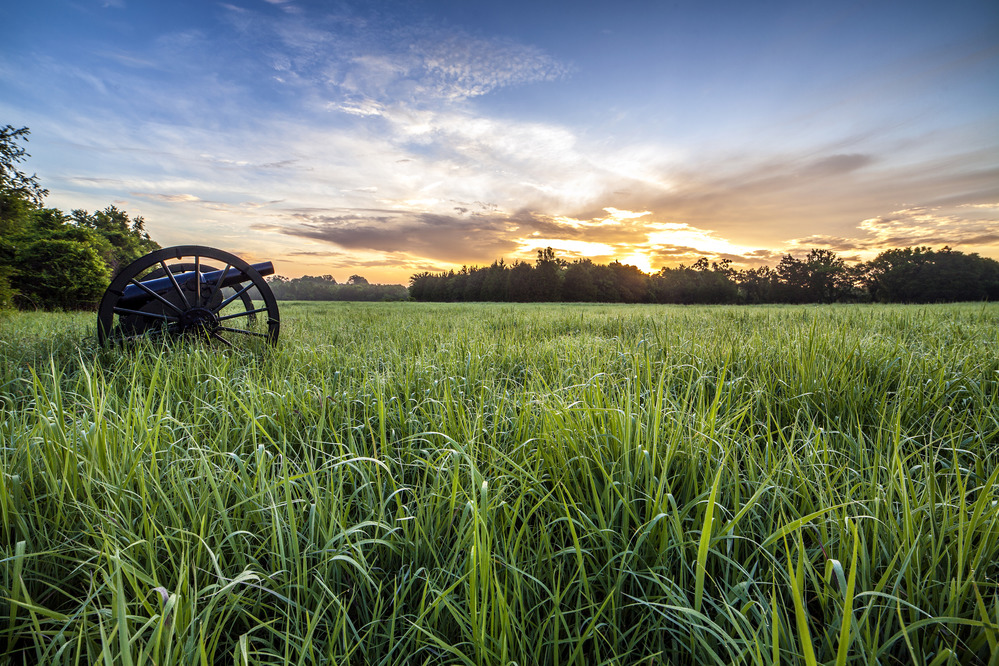 The sun rises over a field with a cannon.