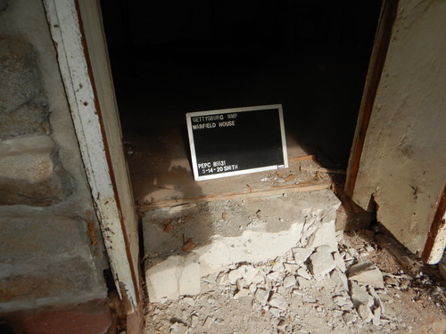 The bottom half of the front door is the focus of the photo. The concrete threshold is broken. A black memo board with picture information is in the center of the photo. It reads, "Gettysburg NMP Warfield House" with the date, photographer, and PEPC number.