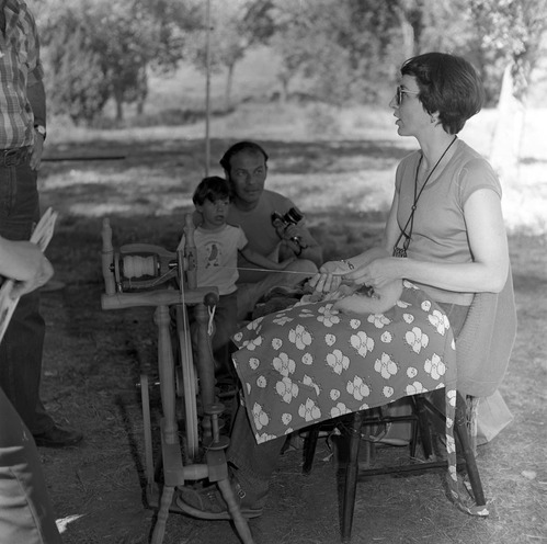 Woman demonstrates spinning wool on a spinning wheel to two men and a child at the first annual Folklife Festival, Zion National Park Nature Center, September 1977.