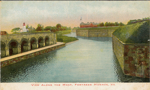 View of the moat of Fort Monroe, Flagstaff Bastion, Old Point Comfort Lighthouse, and Chamberlin Hotel in the background