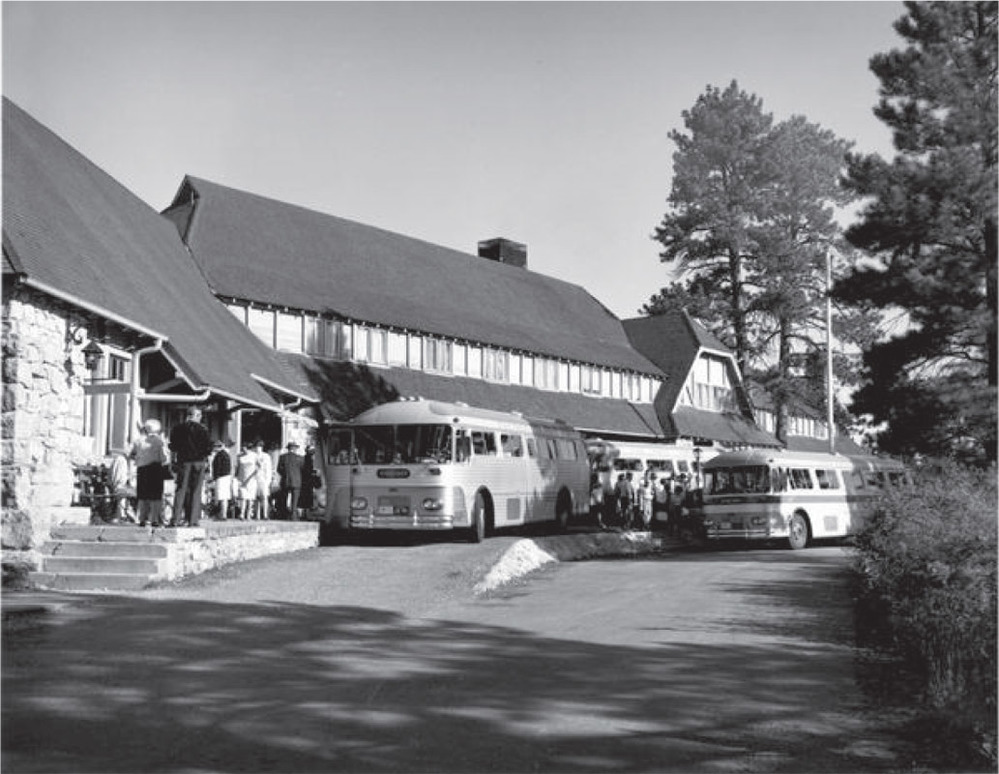 Tour buses from the 1960s line the front of the long lodge, with crowds of visitors gathering around the entrance.