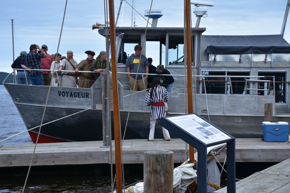 Silver boat full of people near a wooden dock.
