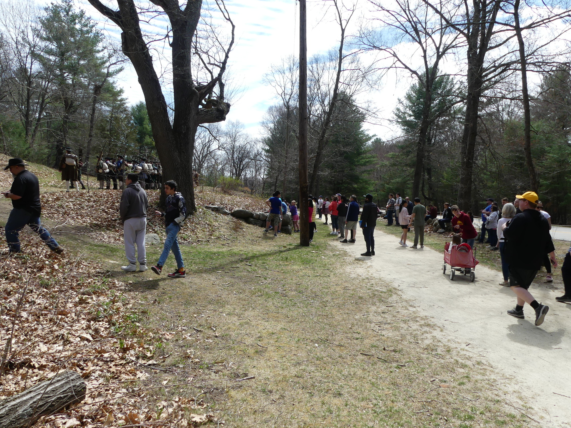 Park visitors walking along Battle Road Trail, militia lining up on the hillside. 