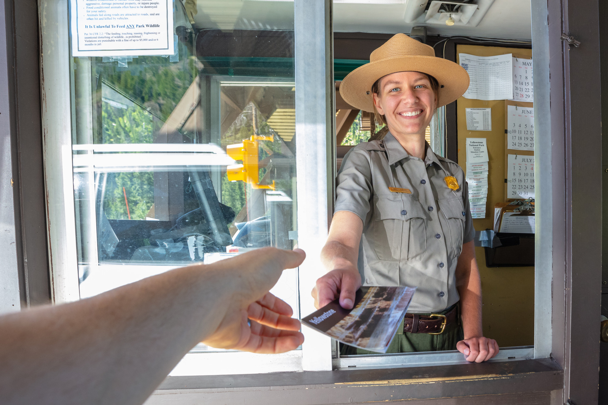 Female ranger smiles while holding out a map to an extended hand from a car.