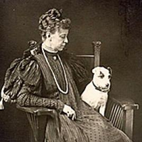 black and white image of white woman sitting in large wooden chair with small white dog