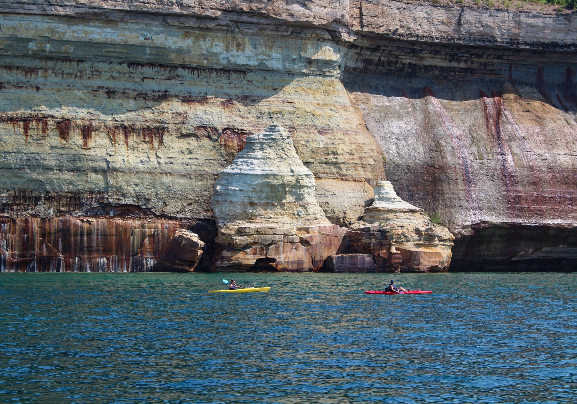 Kayakers paddling along tall cliff faces