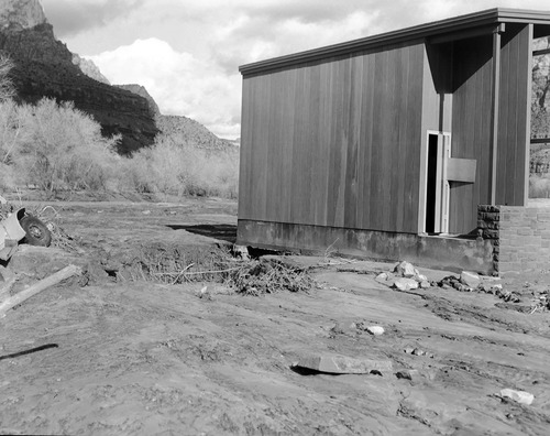 Of December 6, 1966 flood damage - in Watchman campground near amphitheater. Image shows amphitheater, erosion of ground, a corner of a damaged truck and receded water.