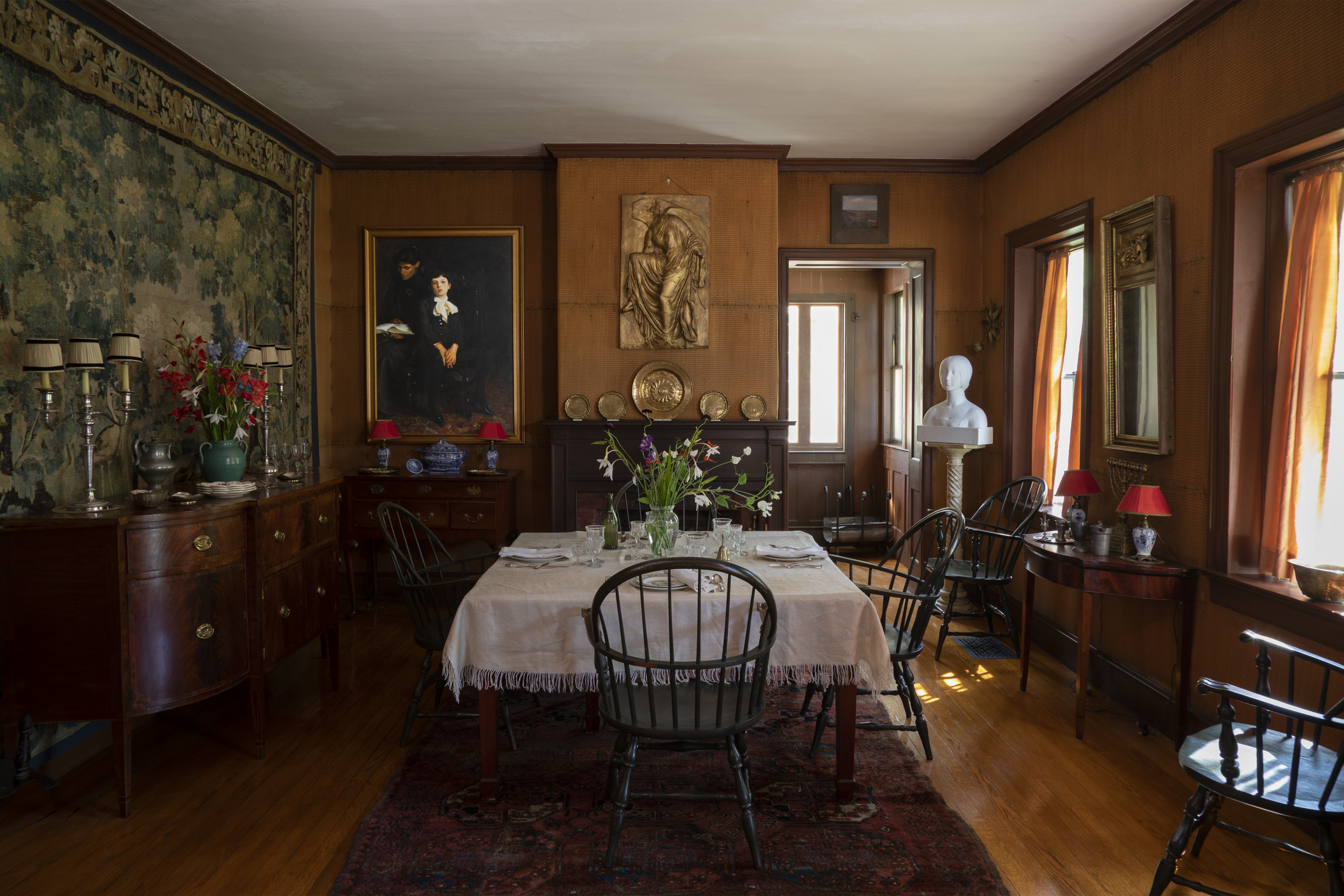 Dining room with square table and four chairs at the center. Art hangs on the wall including a tapestry, painting, and sculptural relief. 