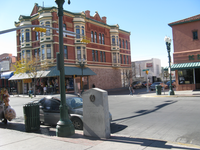 A sunny street scene with historical buildings, shops, pedestrians, and traffic lights in an urban downtown area.