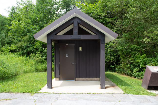 Door has a unisex sign and outside light. An extended roof supported by 2 posts provides shelter.