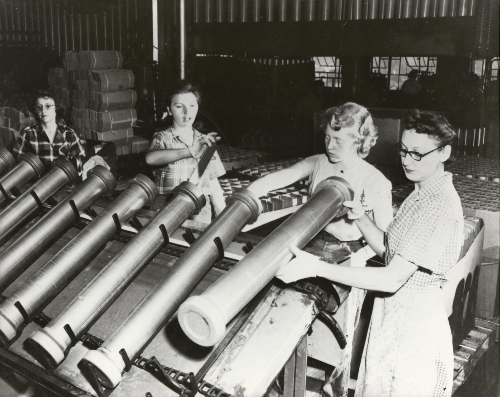 Black and white photo of four women working on an assembly line with large canisters