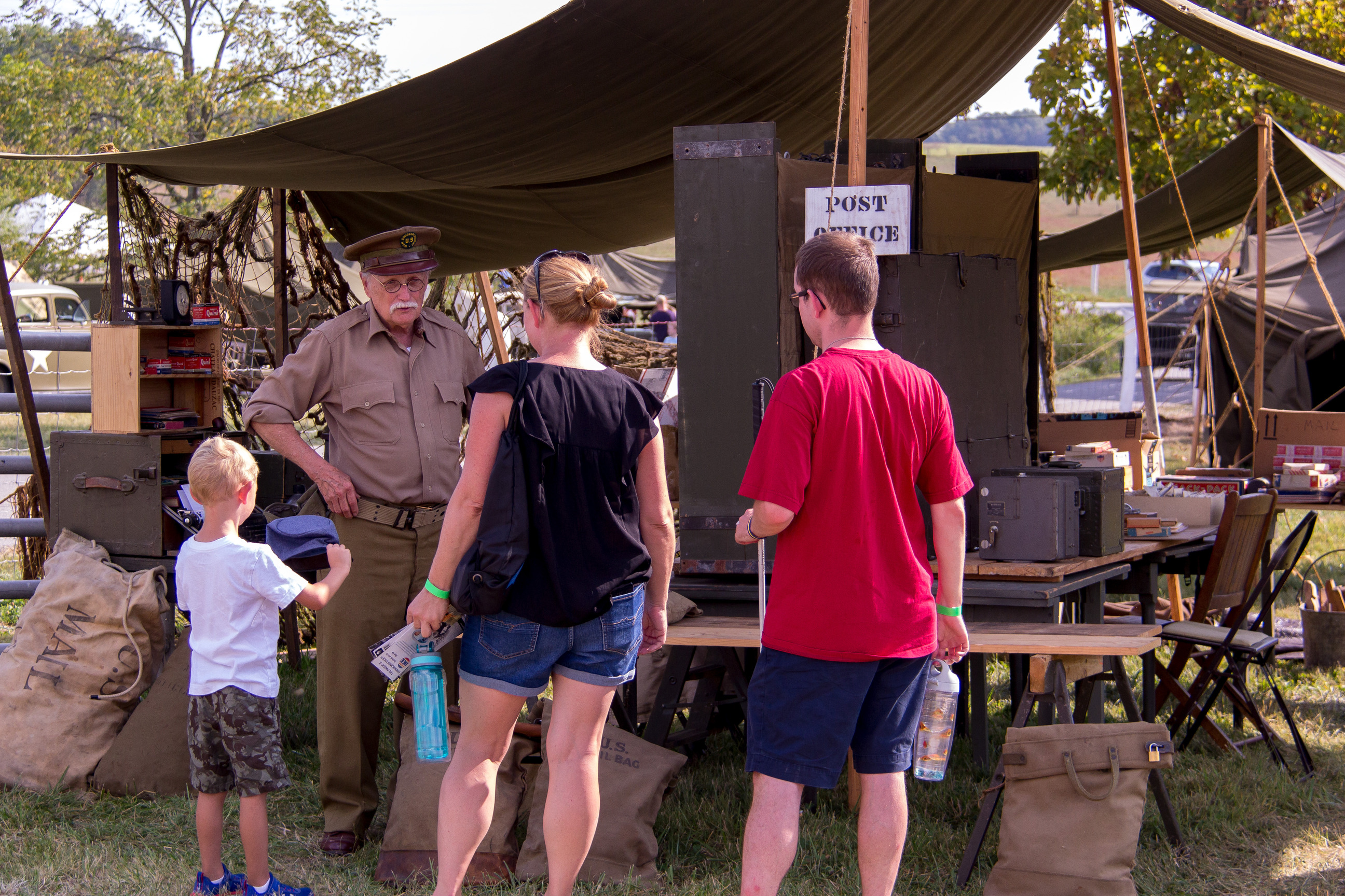 A living historian dressed as an allied World War 2 soldier speaks to a family of visitors in front of an army tent.