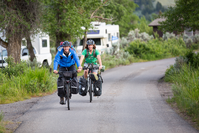 Two bike riders approaching the camera on a small road in a campground.