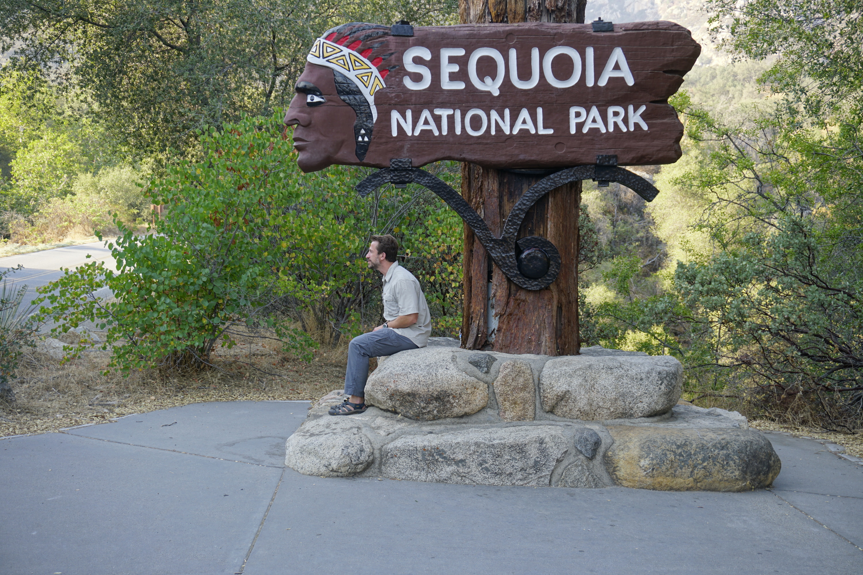 A man sits underneath a brown sign shaped like a persons head. 